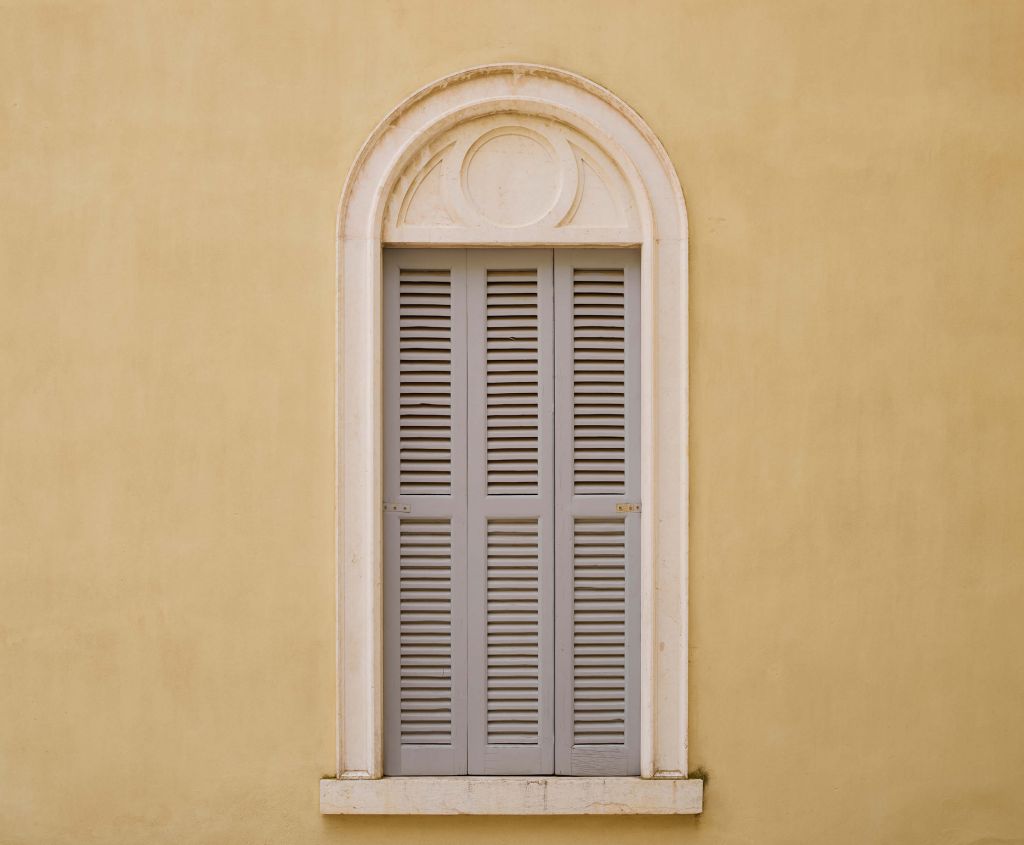 Fenêtre avec volets en bois sur un mur jaune