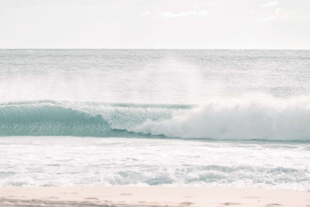 Une vague se brisant sur une plage claire.