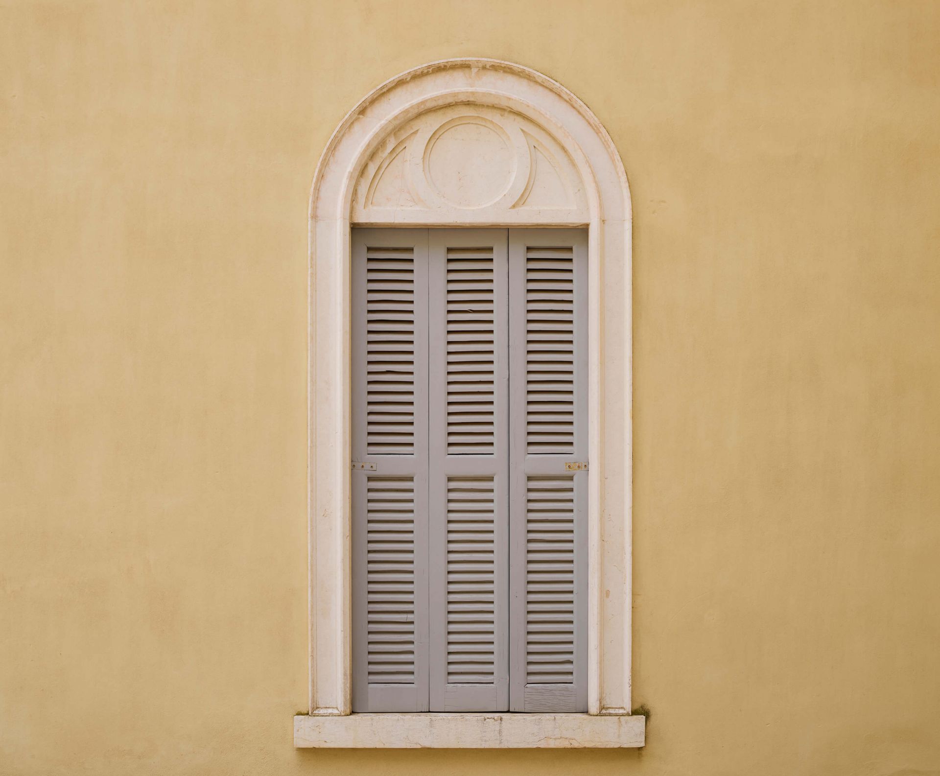 Fenêtre avec volets en bois sur un mur jaune