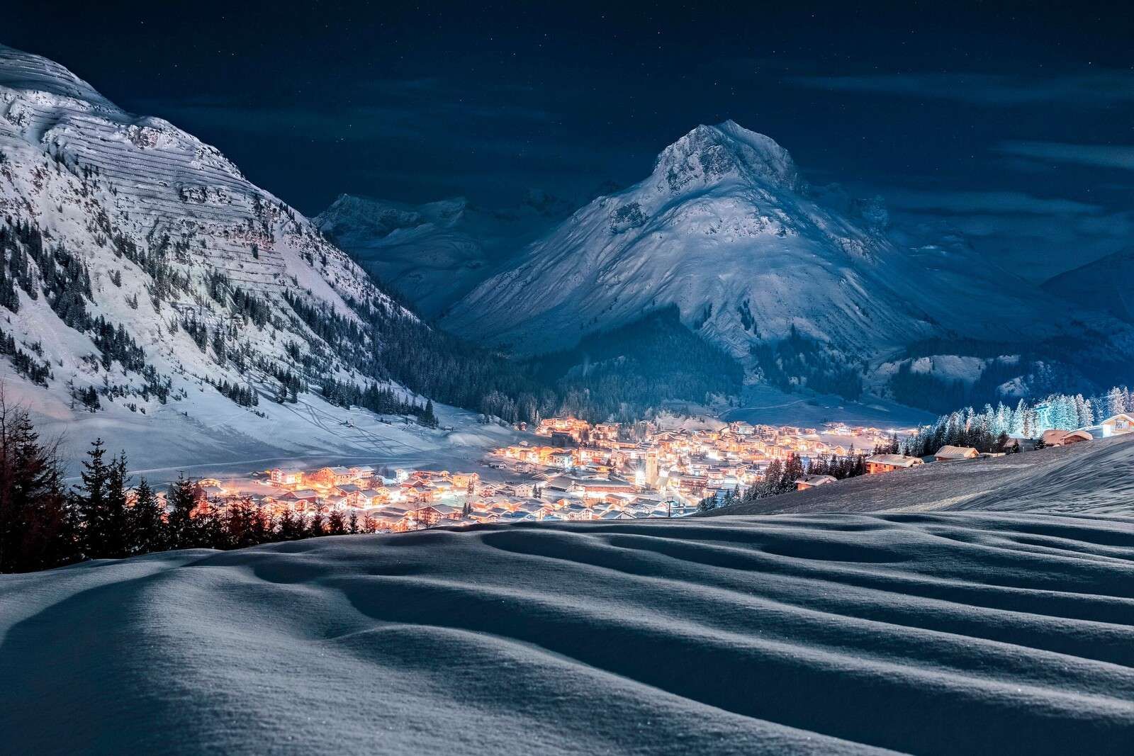 Village d'hiver sous la lumière de la lune dans une vallée alpine.